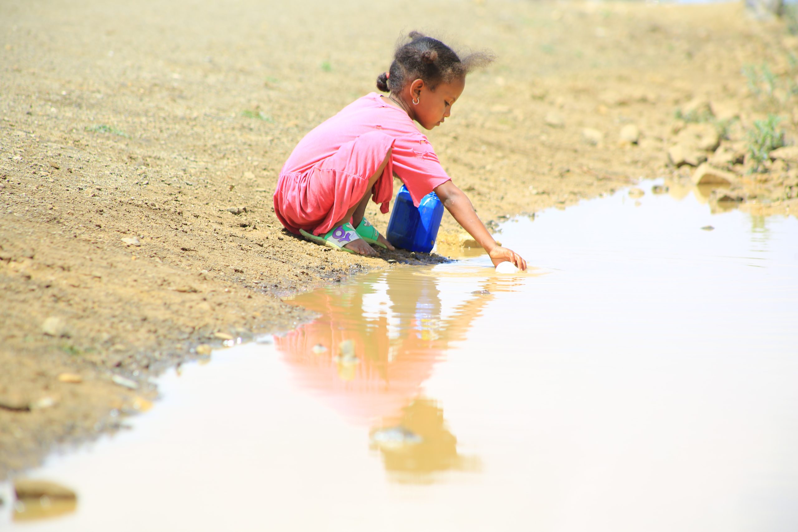 Young girl crouching down and touching a pond with her right hand.